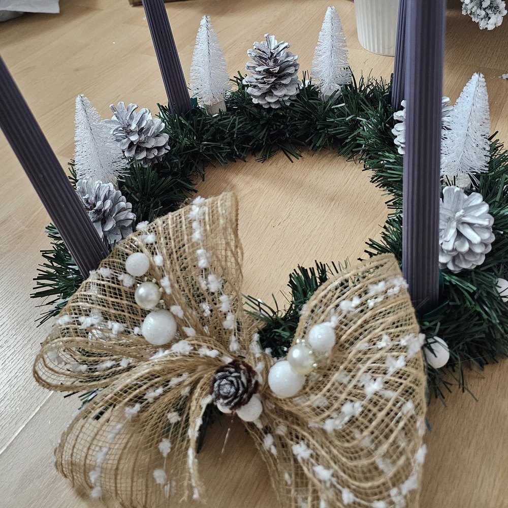 Handmade tabletop advent wreath with four grey taper candles, a burlap bow, flocked pinecones and mini bottle-brush trees
