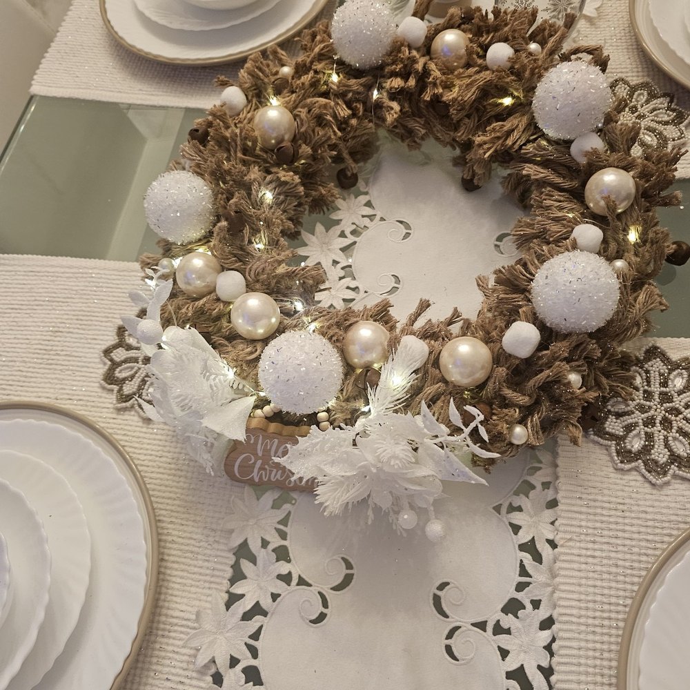 Natural jute wreath of woven rope, pearl and crystal ball ornaments and a white poinsettia, lit with fairy lights